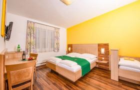 Doppelbett in einem Raum mit dunklem Fu&szlig;boden und gelber R&uuml;ckwand