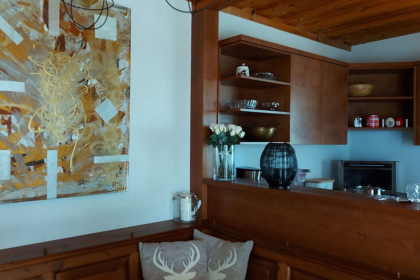 Holzküche mit Kunstwerk an der Wand, Vase mit weißen Rosen und Regalen mit Geschirr.