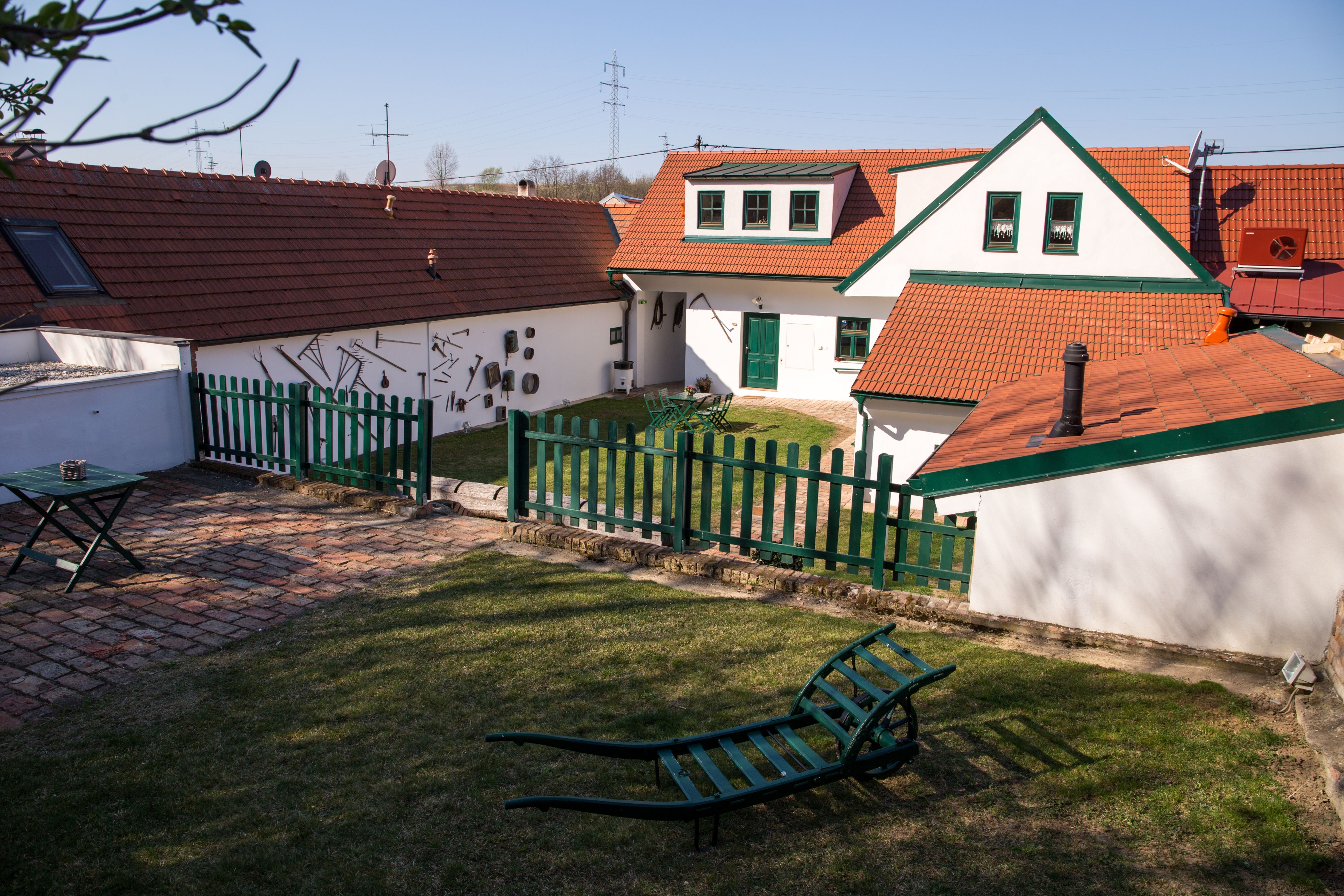 Ein traditioneller Winzerhof mit roten Ziegeldächern, grünen Zäunen und Gartenmöbeln auf einer Wiese.