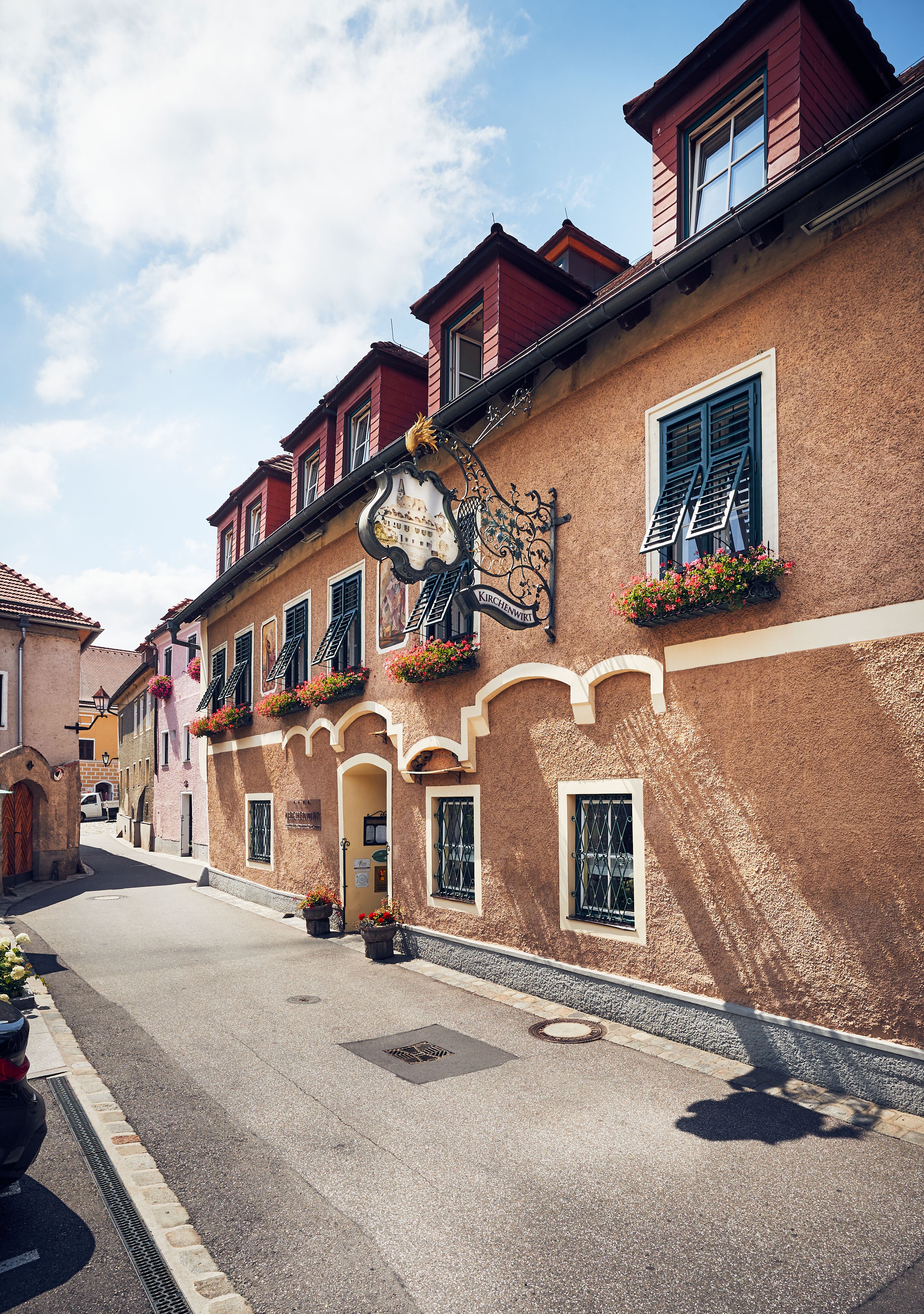 Ein gelbes Gebäude mit roten Dächern am Flussufer, umgeben von Bäumen.