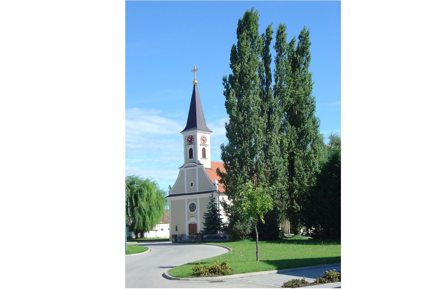 Eine Kirche mit Turm und Uhr vor blauem Himmel, umgeben von Bäumen.