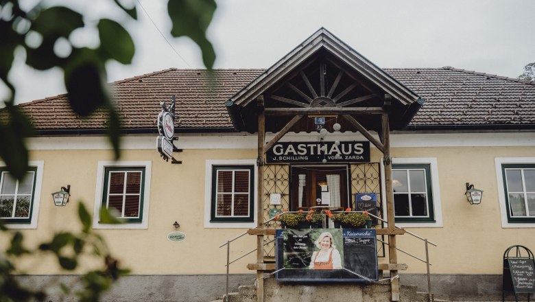 Eingang eines traditionellen Gasthauses mit Holzveranda und Werbetafel.
