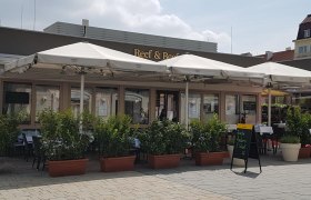 Au&szlig;enansicht eines Restaurants mit Schanigarten und Sonnenschirmen.