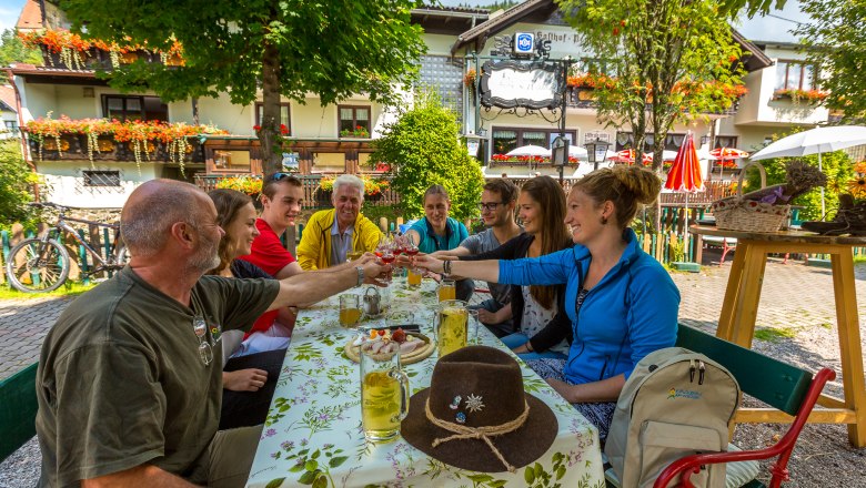 Gruppe von Menschen st&ouml;&szlig;t in einem Gastgarten an.