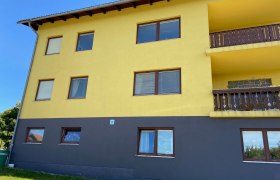 Gelbes Gebäude mit braunen Fenstern und Balkonen, blauer Himmel im Hintergrund.