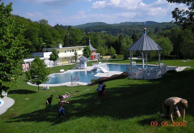 Ein Freibad mit Badeg&auml;sten auf einer Wiese und einem Pavillon im Hintergrund.