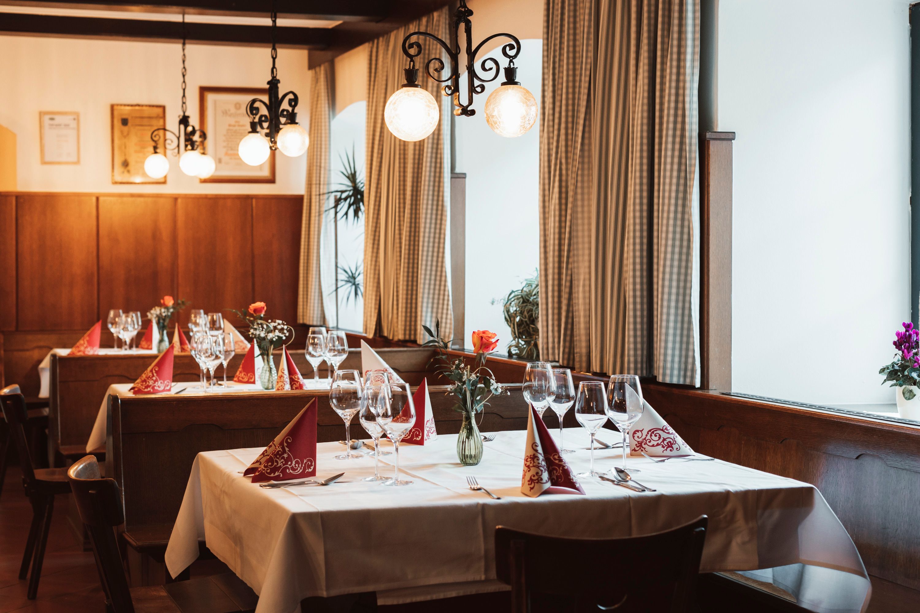 Gemütliches Restaurant mit gedeckten Tischen, Weingläsern und Blumenvasen.