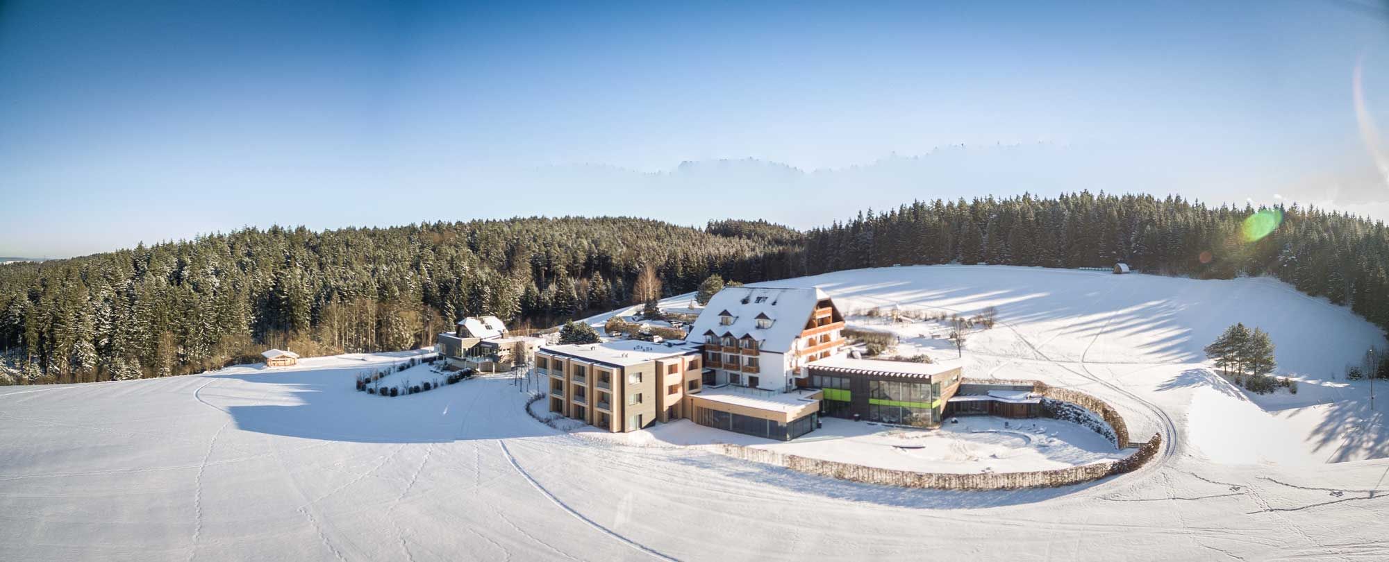 Winterlandschaft mit Hotel Schwarz Alm, umgeben von schneebedeckten Feldern und Wäldern.