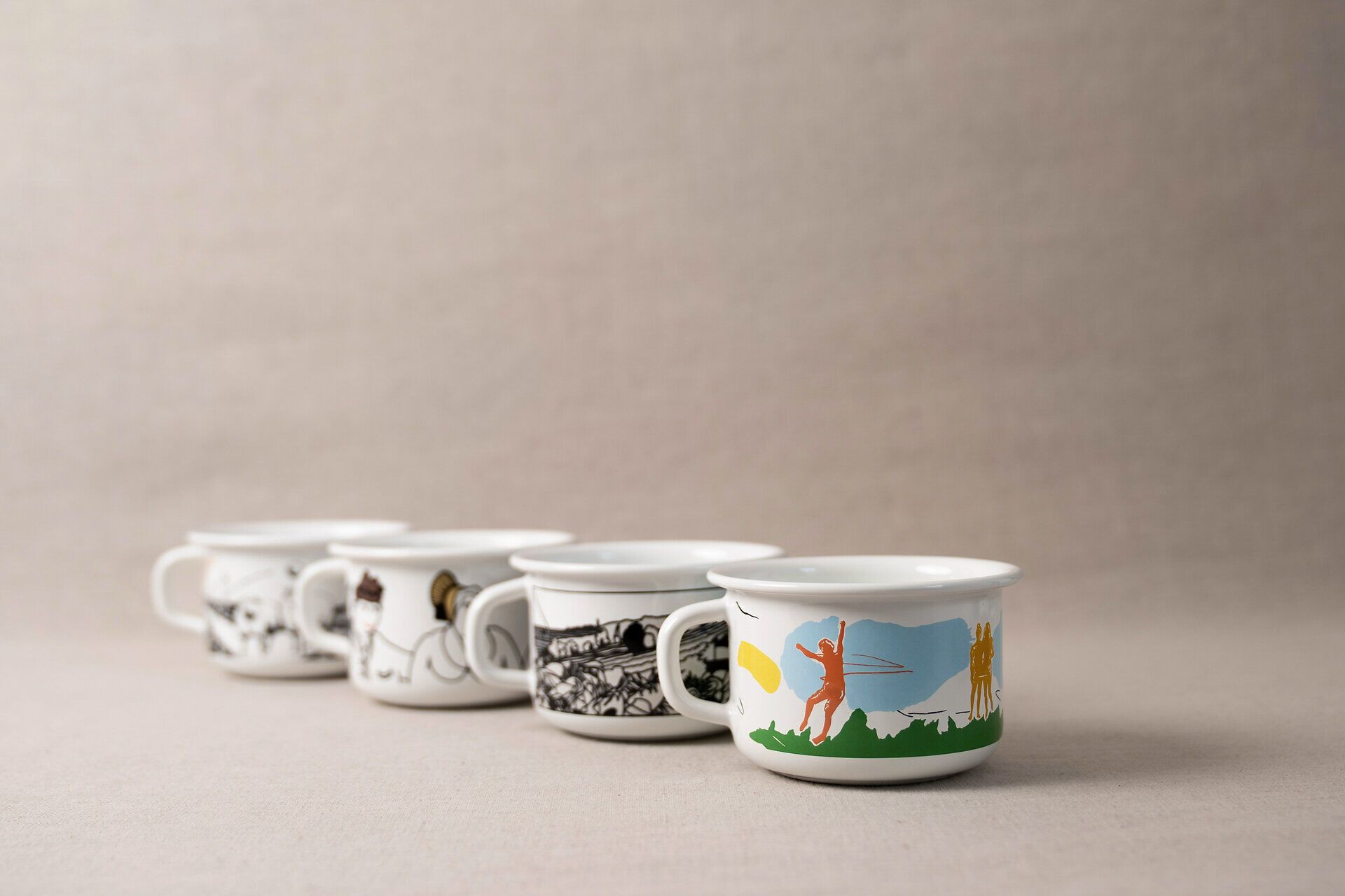 4 von Küstler:innen gestaltete Tassen aus Email von der Firma Riess mit aus Niederösterreich inspirierten Motiven. 