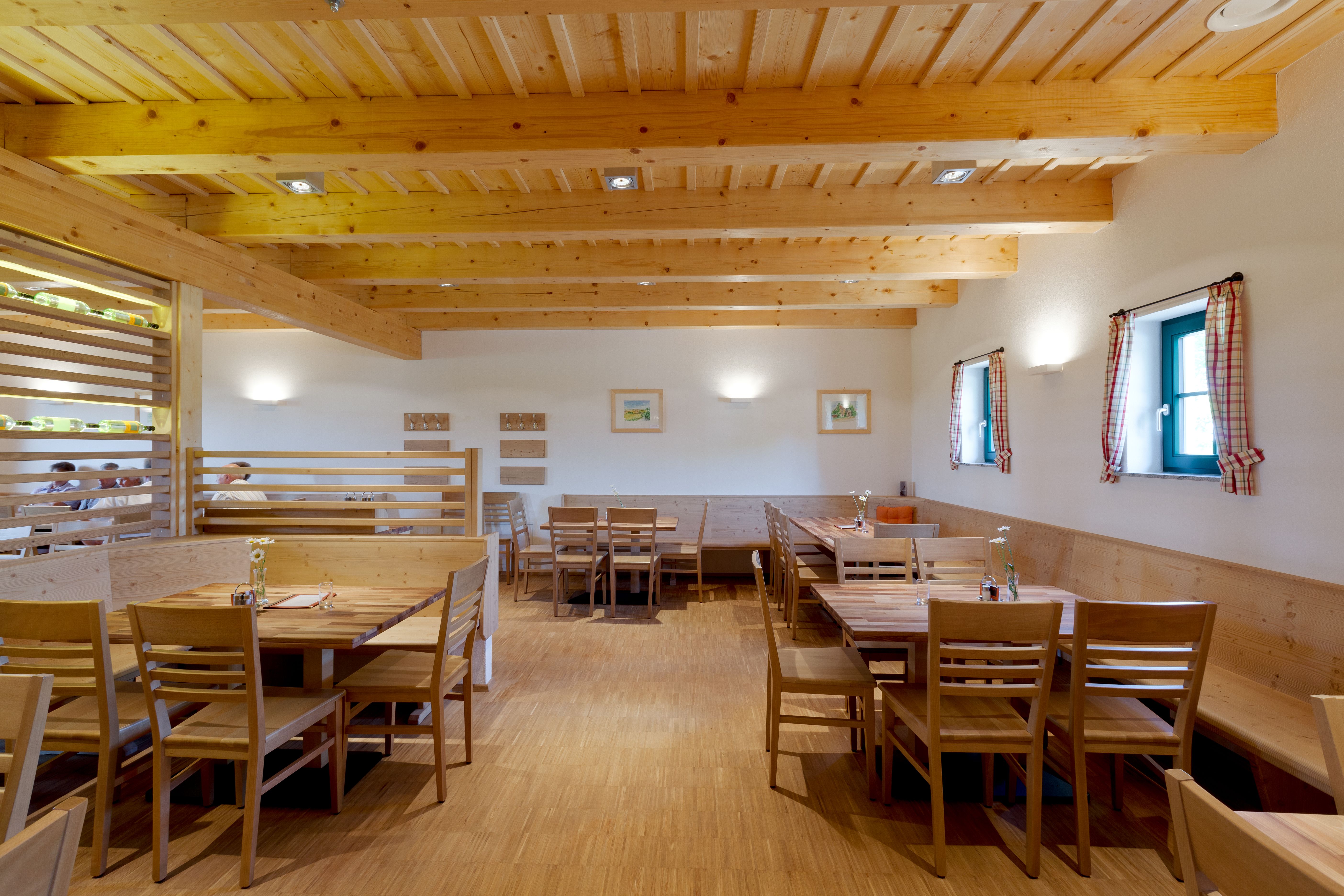 Innenansicht eines gemütlichen Gastraums mit Holzmöbeln und Holzbalkendecke.