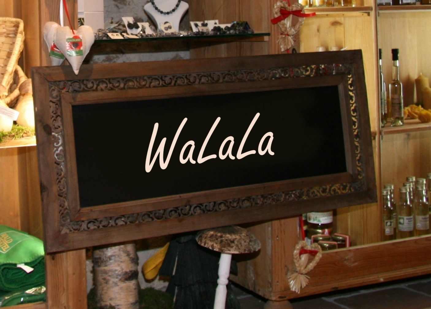 Ein dekoratives Holzschild mit der Aufschrift 'WaLaLa' in einem rustikalen Laden mit Regalen voller Produkte.