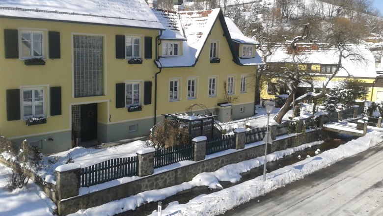 Pension Hendling, © Josef Hendling Gelbes Haus im Winter mit Schnee bedeckt, umgeben von einem Zaun und Bäumen.