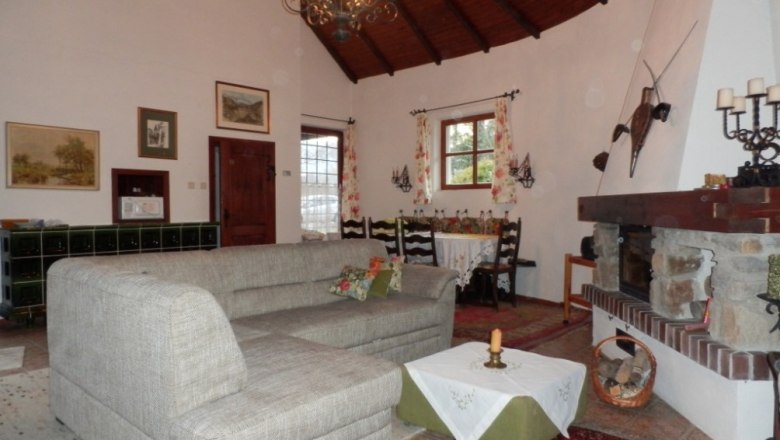 Gem&uuml;tliches Wohnzimmer mit grauem Sofa, Kamin und Esstisch. Rustikale Dekoration und Holzbalkendecke.