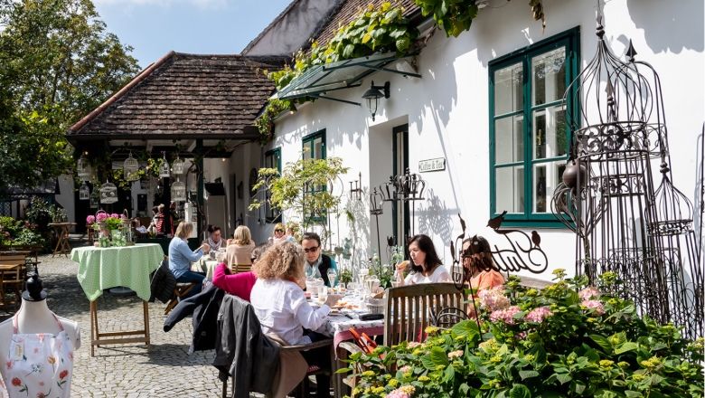Menschen sitzen an Tischen im Freien eines gemütlichen Hofes.