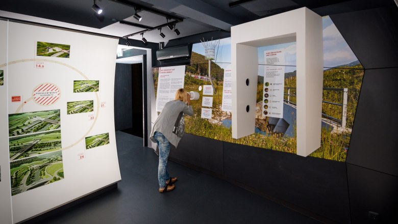 Eine Person betrachtet eine Ausstellung in einem modernen Informationszentrum mit Bildern und Texten an den Wänden.