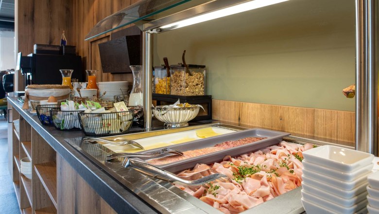 Frühstücksbuffet mit Aufschnitt, Käse, Müsli und Getränken.