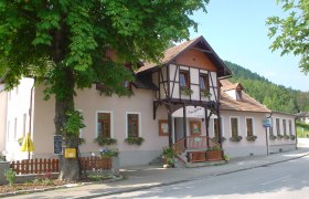 Traditionelles Gasthaus, davor Blumenkästen, umgeben von Bäumen.