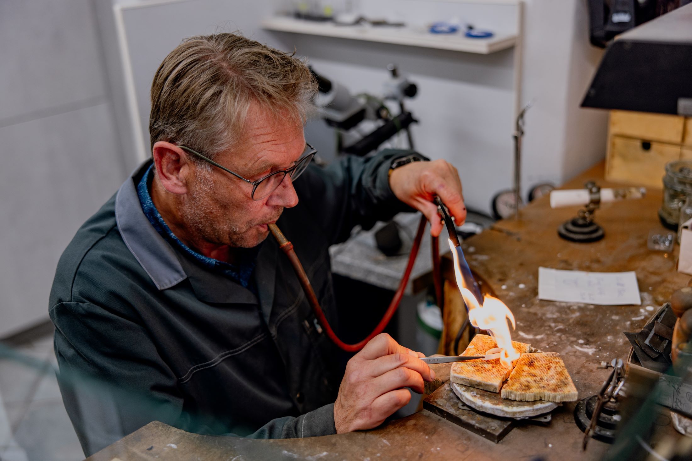 Ein Mann arbeitet mit einem Brenner an einem Schmuckstück in einer Werkstatt.