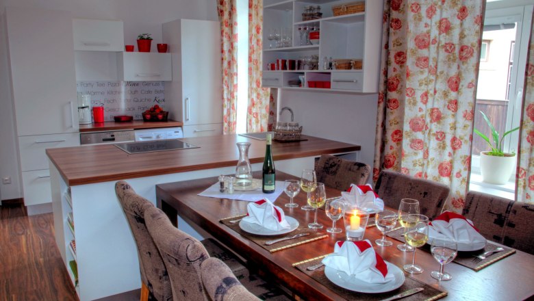 Moderne K&uuml;che mit Esstisch, gedeckt mit Gl&auml;sern und Servietten, Blumenmuster-Vorh&auml;nge.