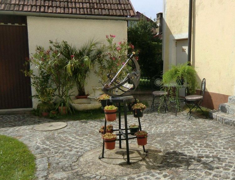 Ein sonniger Innenhof mit Sonnenuhr, Pflanzen und Gartenmöbeln.