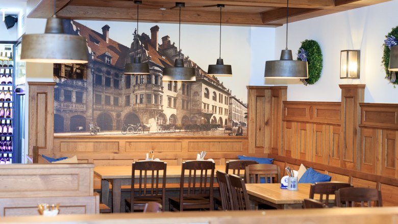 Innenansicht eines traditionellen bayerischen Restaurants mit Holzmöbeln und Wandbild des Hofbräuhauses.