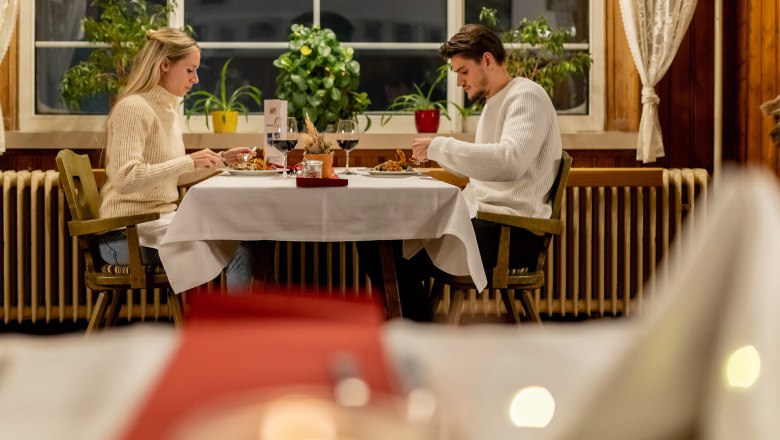 Paar sitzt sich in gem&uuml;tlichem Raxalm-Berggasthof gegen&uuml;ber und isst gemeinsam bei Kerzenlicht.