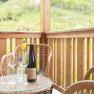 Ein Balkon mit Holzmöbeln, einer Weinflasche und Gläsern auf einem Tisch. Im Hintergrund grüne Landschaft.