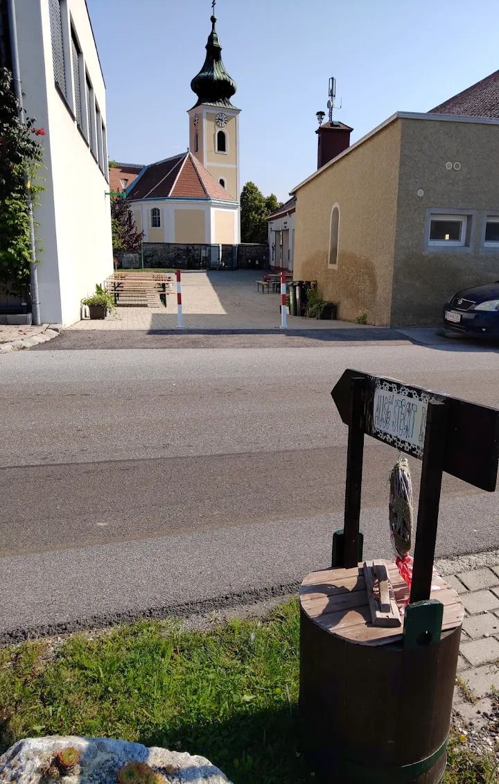 Buschenschank Thaller Wolfsthal, Blick in den Innenhof mit Heurigentischen, im Hindergrund sieht man eine Kirche 