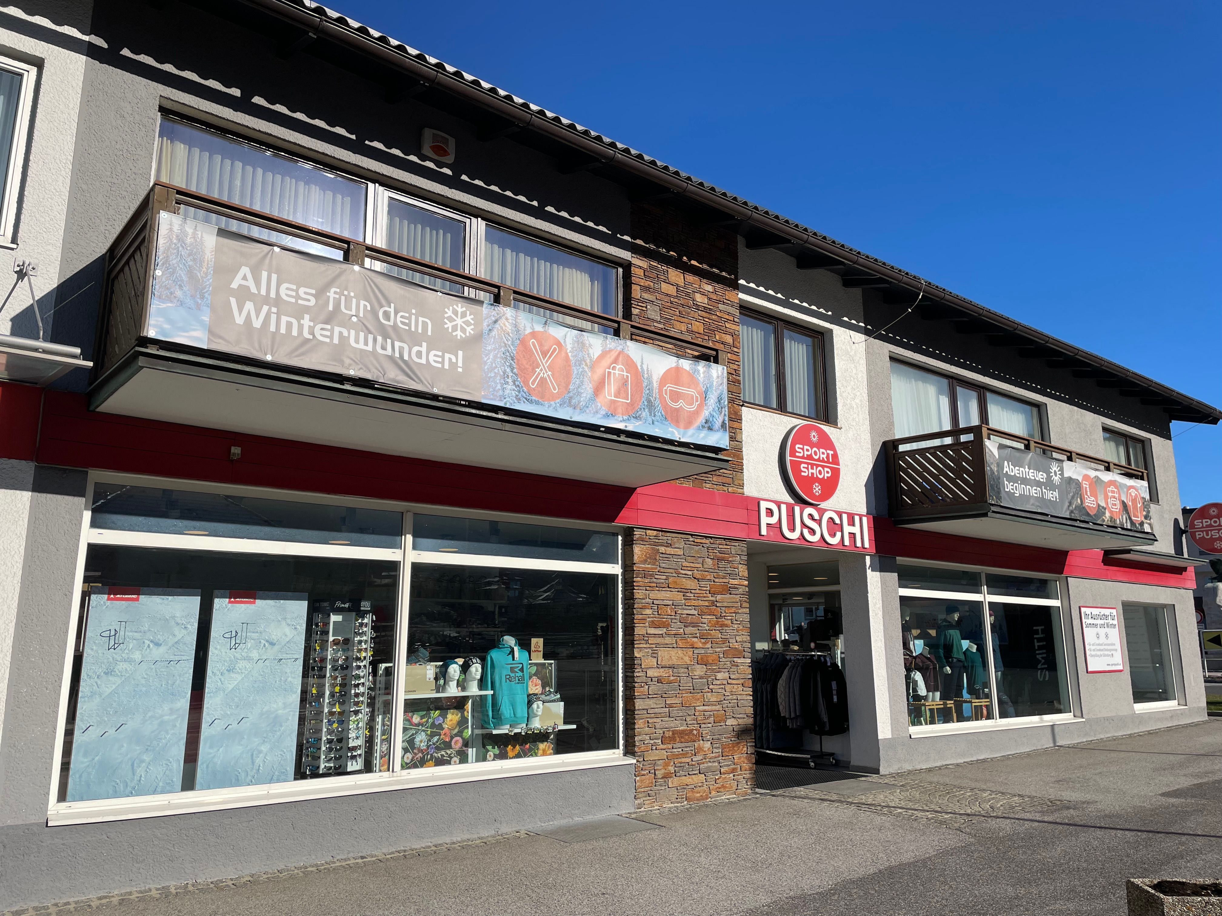 Außenansicht eines Sportgeschäfts namens Puschi mit großen Fenstern und Werbebannern für Winterausrüstung.