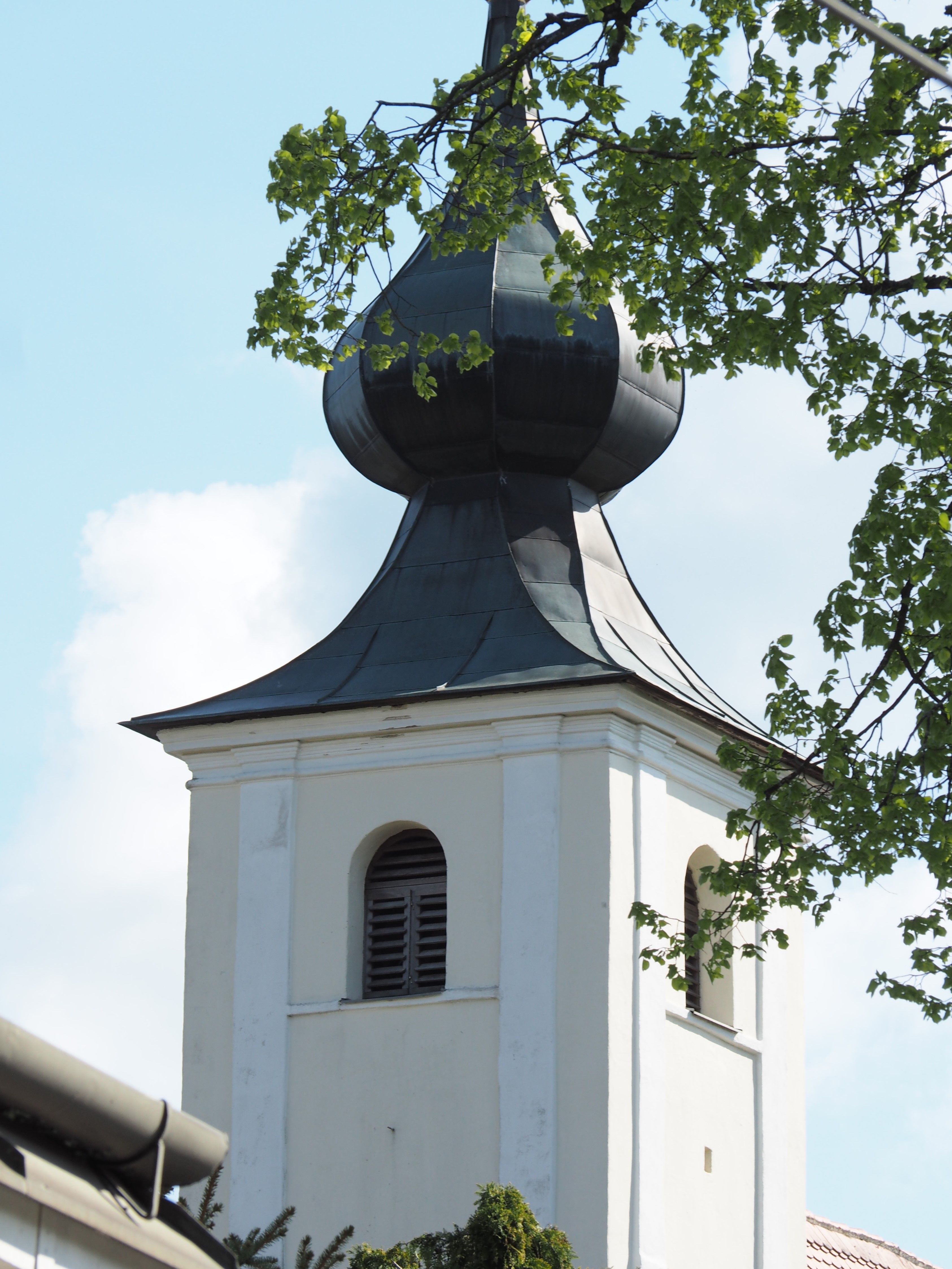 Kirchturm mit Zwiebelhaube und grünen Blättern im Vordergrund.