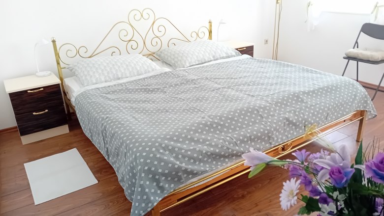 Schlafzimmer mit einem Doppelbett, goldfarbenem Kopfteil, zwei Nachttischen und Blumen im Vordergrund.