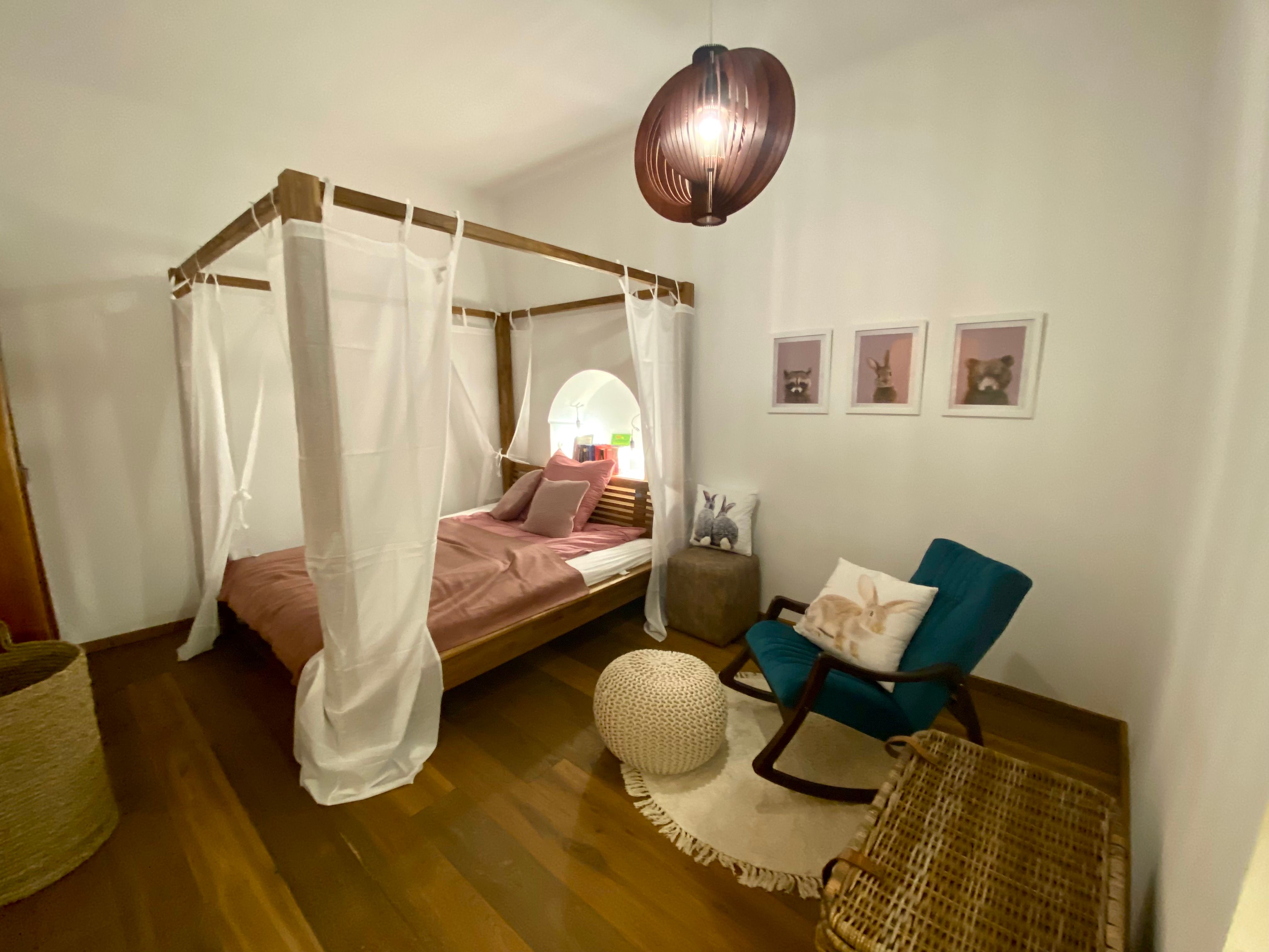 Gemütliches Schlafzimmer mit Himmelbett, Schaukelstuhl und Tierbildern an der Wand.