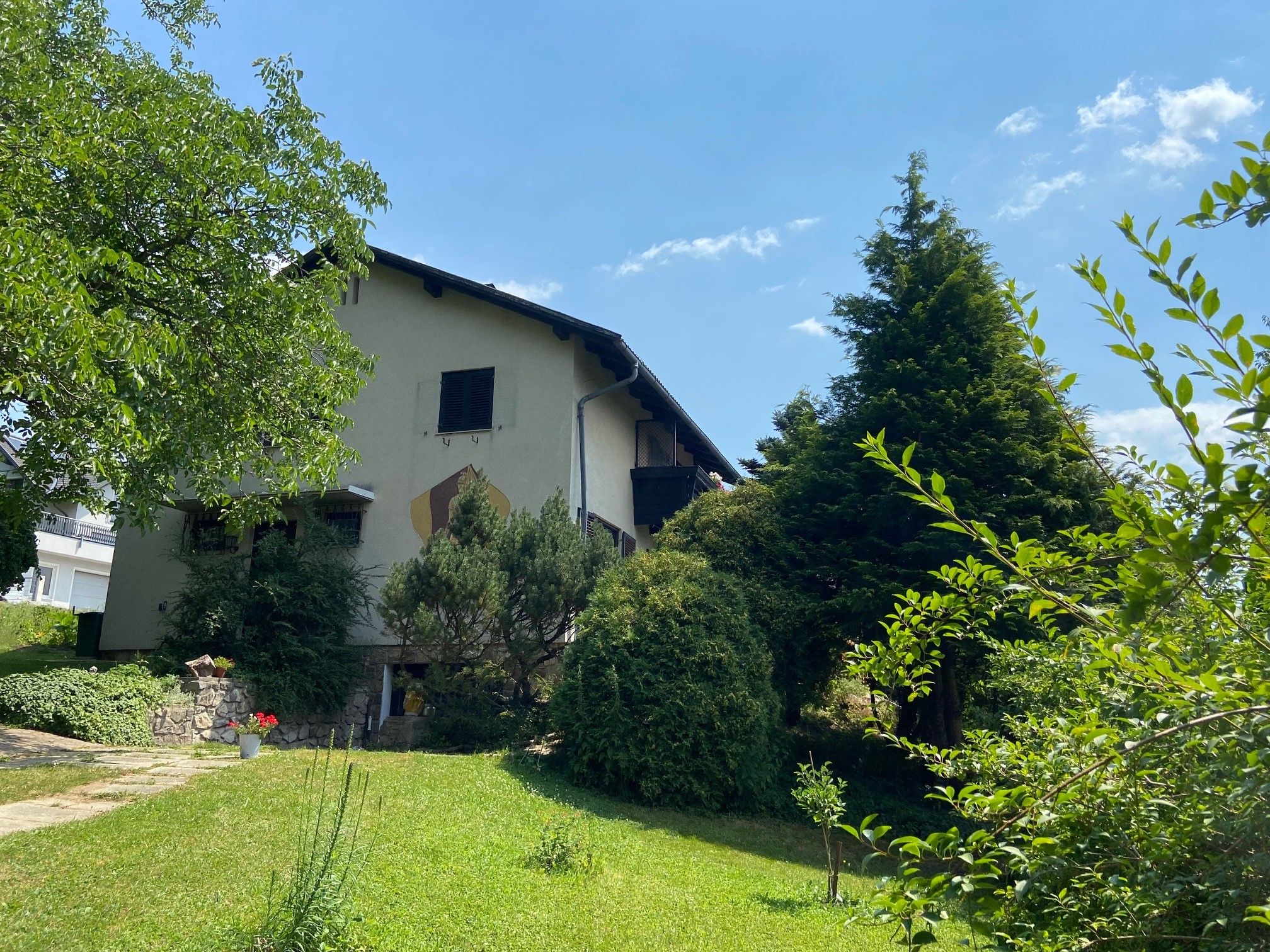 Ein zweistöckiges Haus mit Garten und Bäumen, bei sonnigem Wetter.