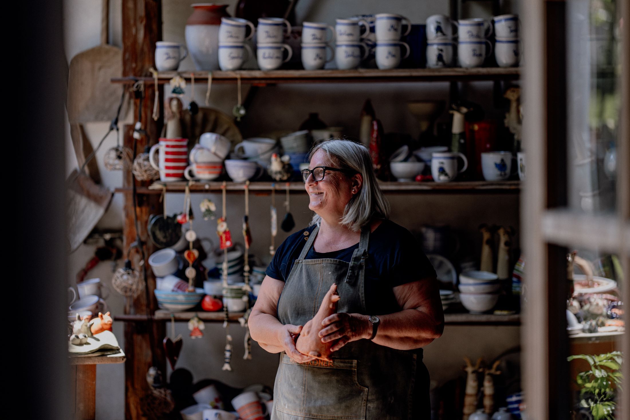 Eine Frau in einer Töpferwerkstatt, umgeben von Keramikgeschirr und Dekorationen.