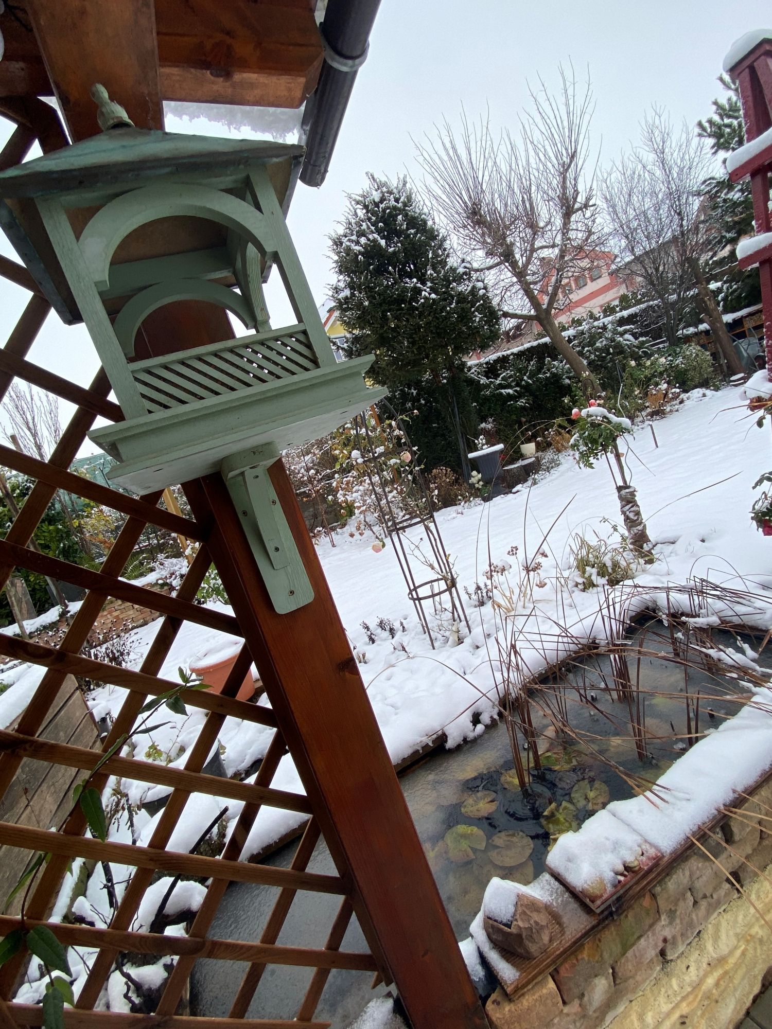 Verschneiter Garten mit Vogelhaus und Teich.