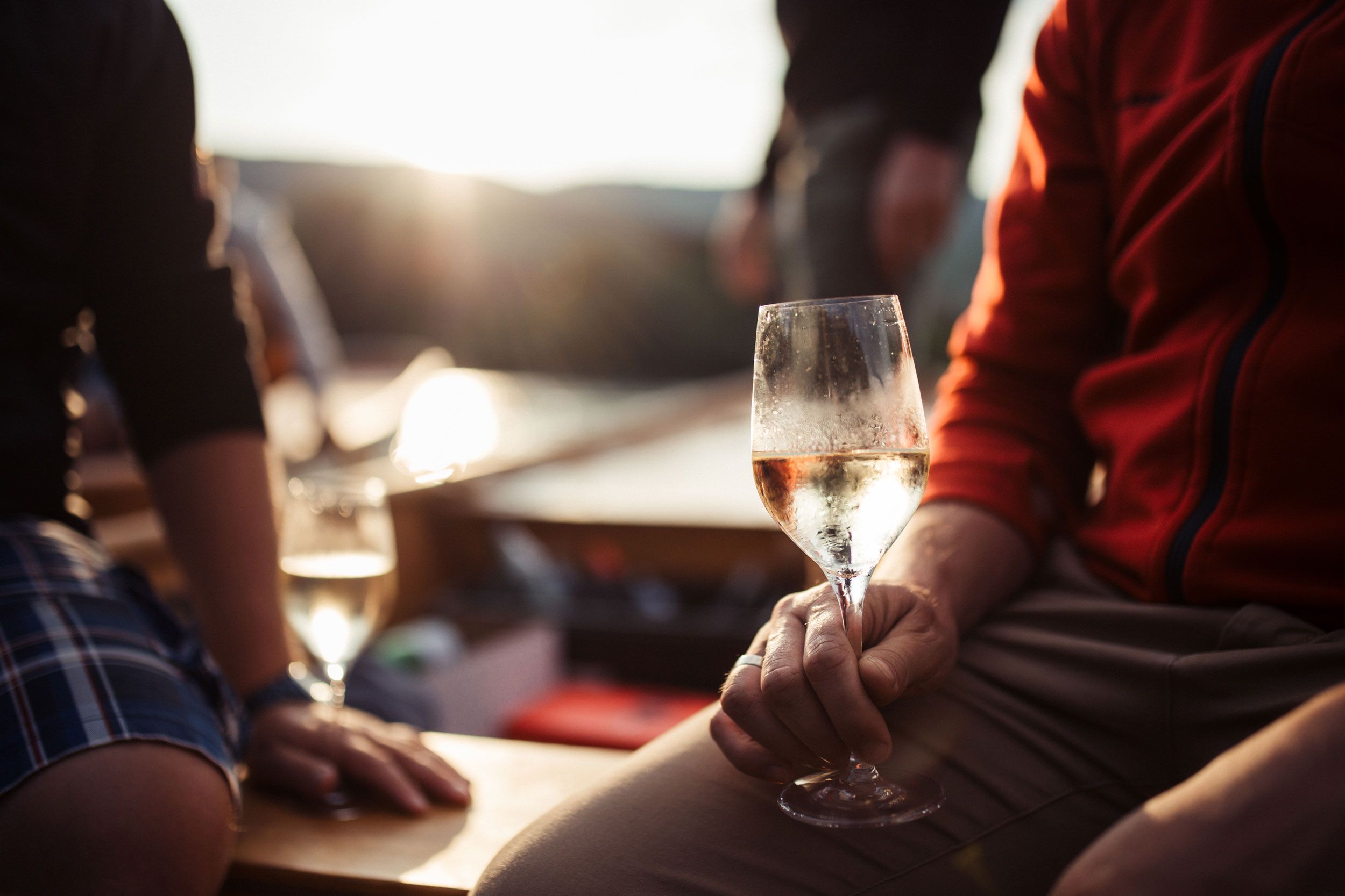 Person hält ein Weinglas in der Hand, im Hintergrund Sonnenuntergang.