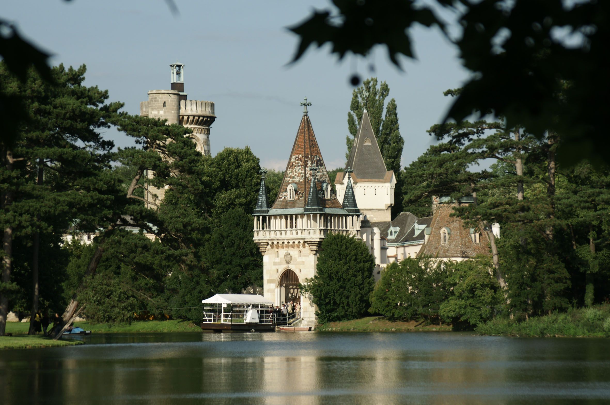 Schloss Laxenburg mit Türmen und Bäumen am Seeufer.
