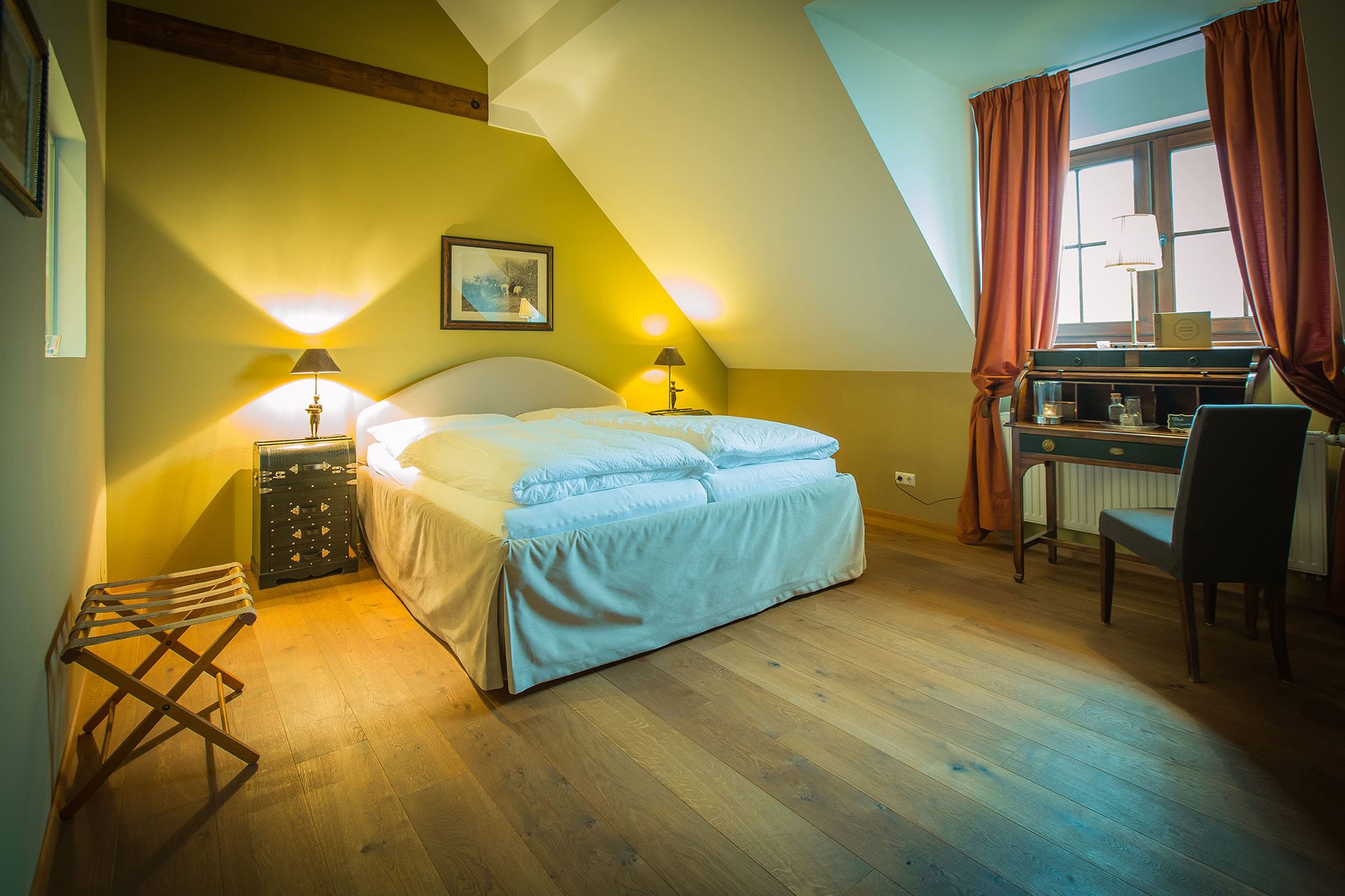 Gemütliches Doppelzimmer mit Holzboden, Doppelbett, Schreibtisch und Fenster mit Vorhängen.