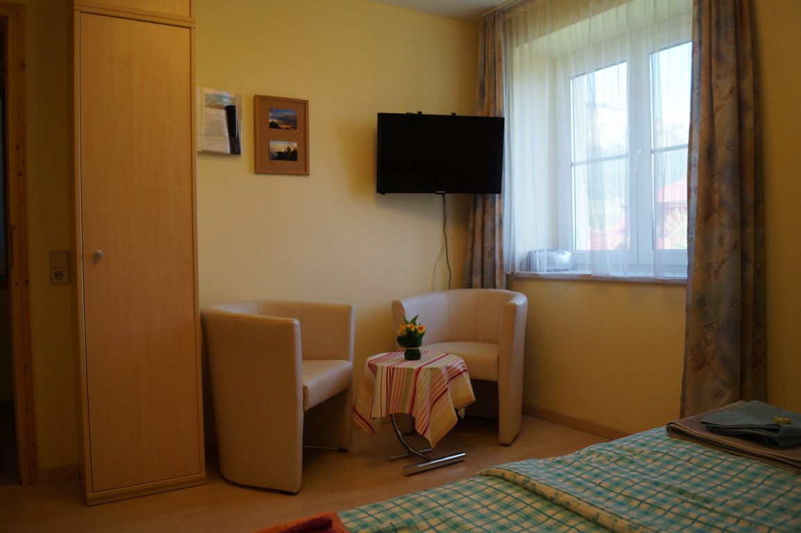 Gemütliche Sitzecke mit zwei Sesseln, kleinem Tisch und Fernseher in einem hellen Raum mit Fenster.