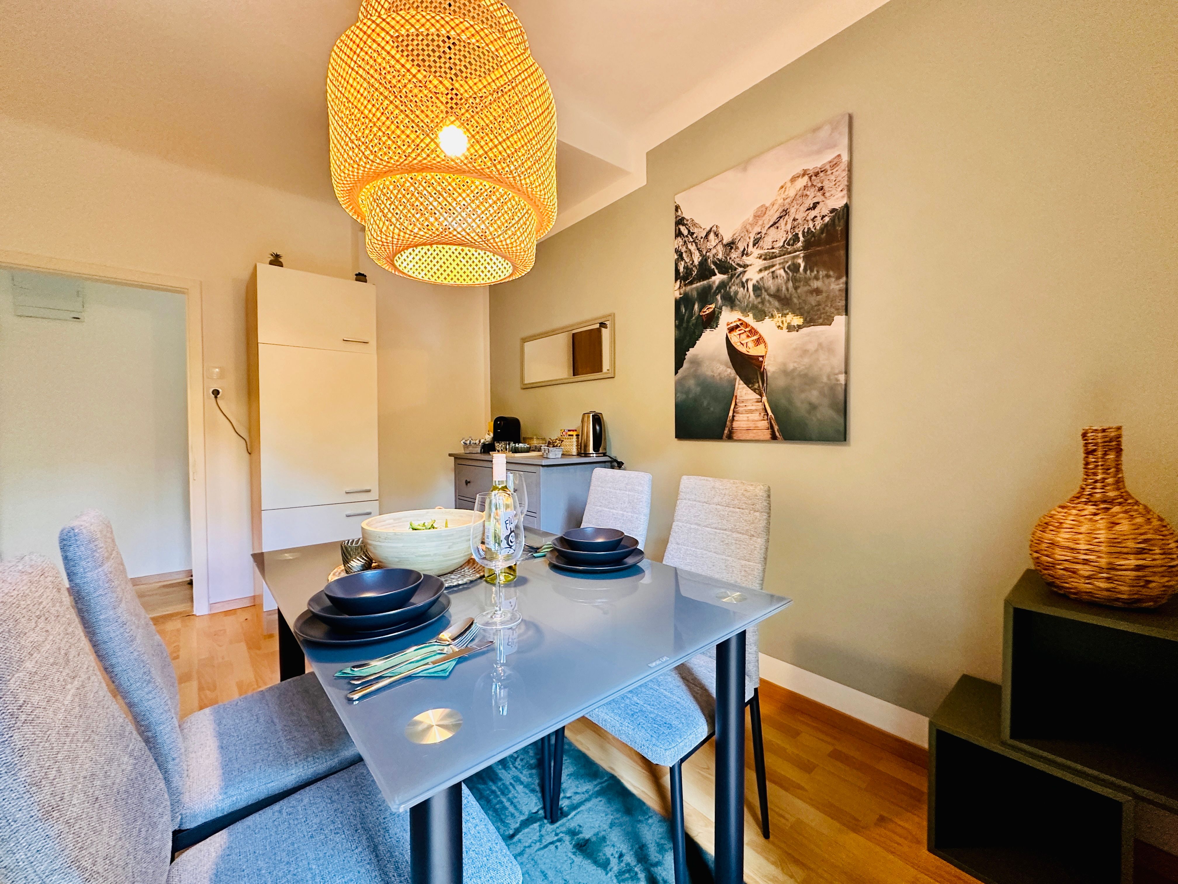 Esszimmer mit Glastisch, grauen Stühlen und großem Lampenschirm.