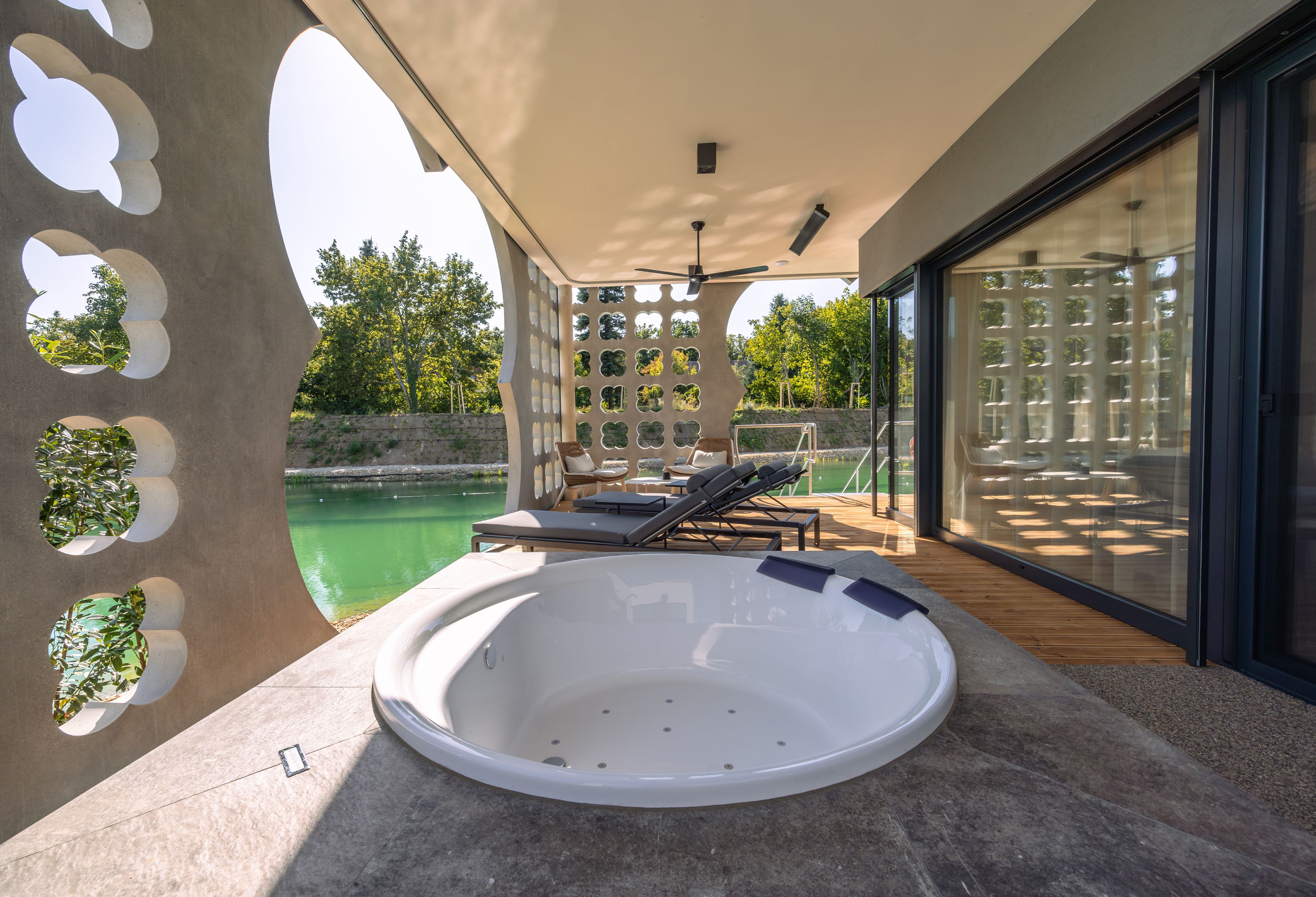 Terrasse mit Whirlpool und Liegestühlen, Blick auf einen Teich.