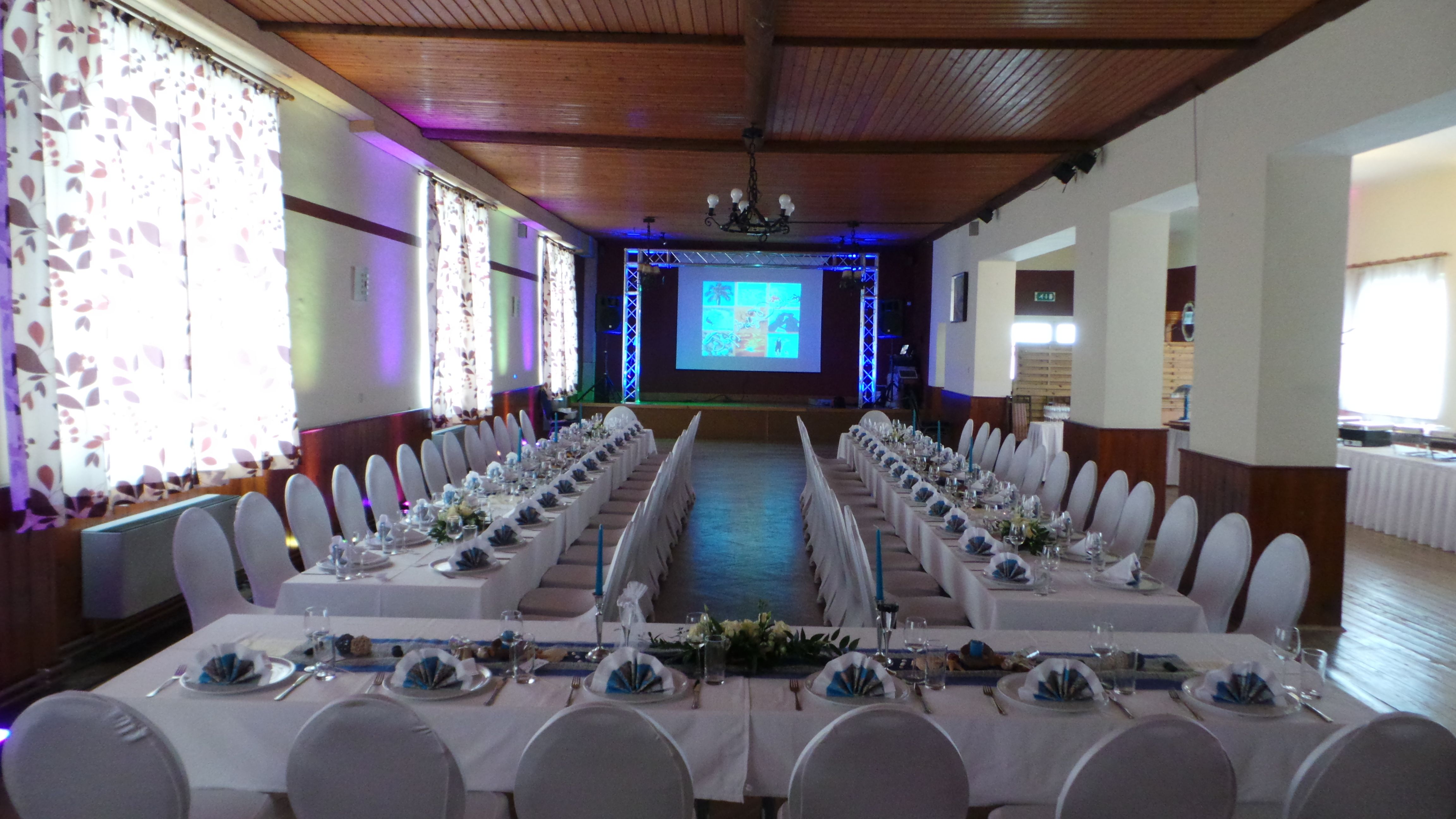 Festlich gedeckter Saal mit langen Tafeln und Projektionsleinwand.