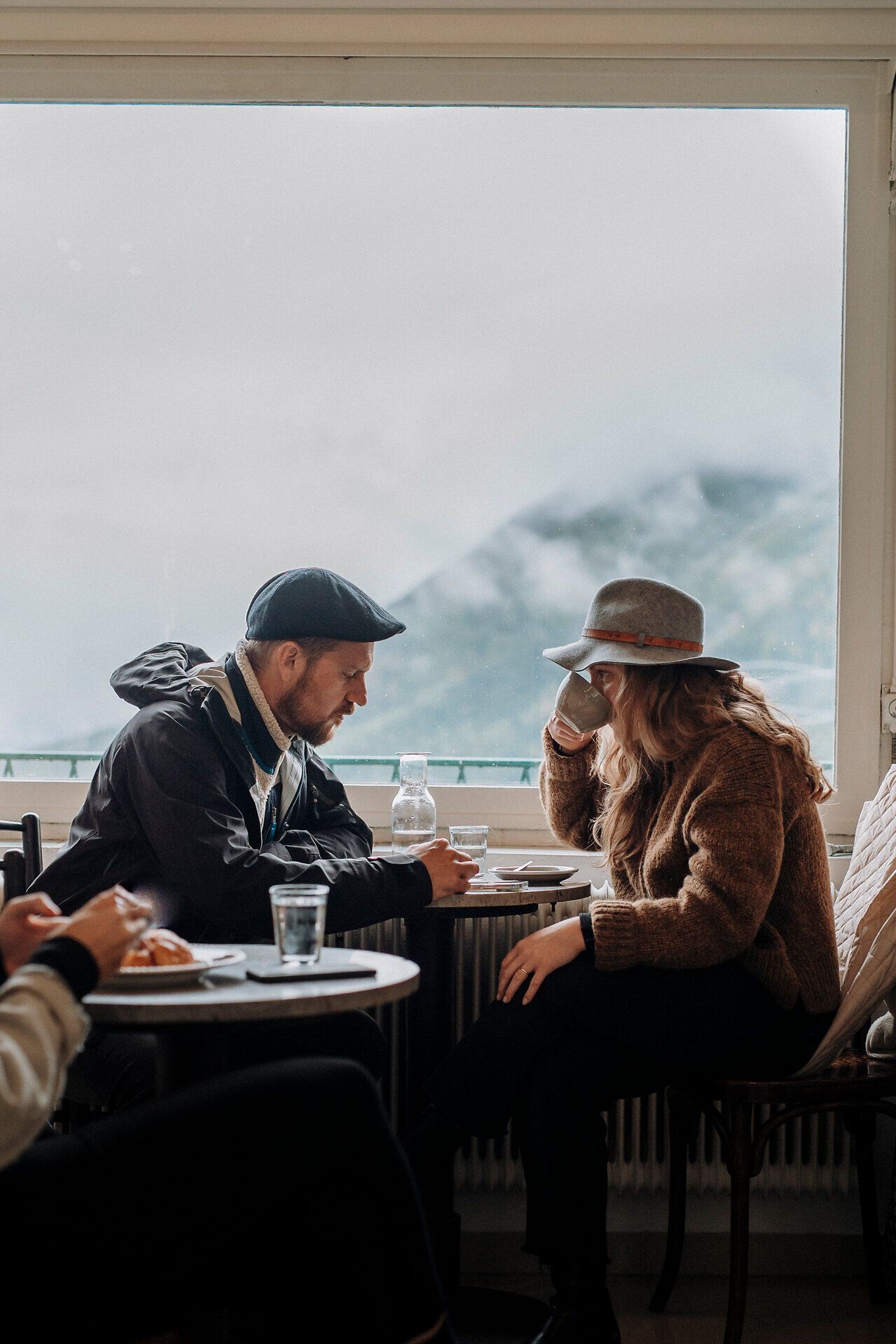 In einem gemütlichen Café am Semmering genießen zwei Gäste eine Tasse Kaffee und die atemberaubende Aussicht auf die umliegenden Berge. Die entspannte Atmosphäre und die sanften Klänge der Natur laden dazu ein, den Moment in vollen Zügen auszukosten.