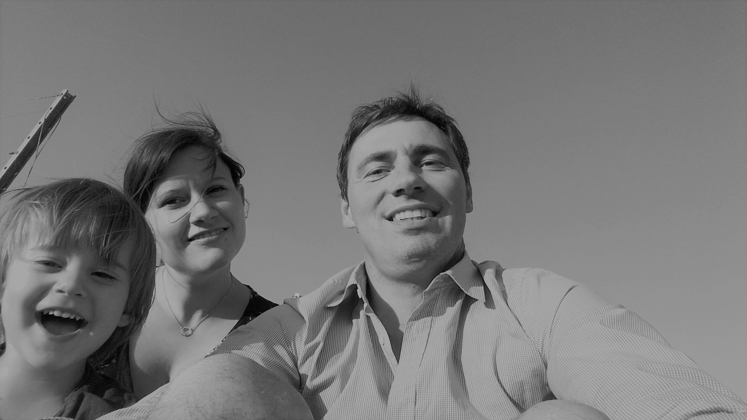 Schwarz-weiß Foto einer lächelnden Familie, bestehend aus einem Mann, einer Frau und einem Kind, die in die Kamera schauen.