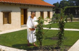 Ein Mann in antiker Kleidung steht in einem Garten vor einem historischen Geb&auml;ude.