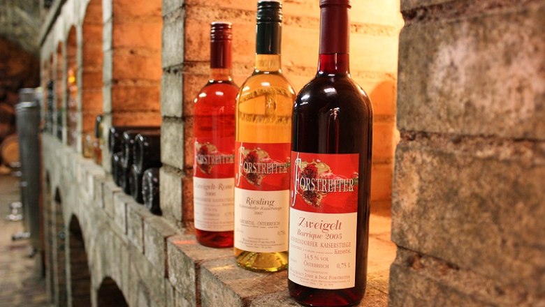 Drei Weinflaschen im Weinkeller auf einem Regal.