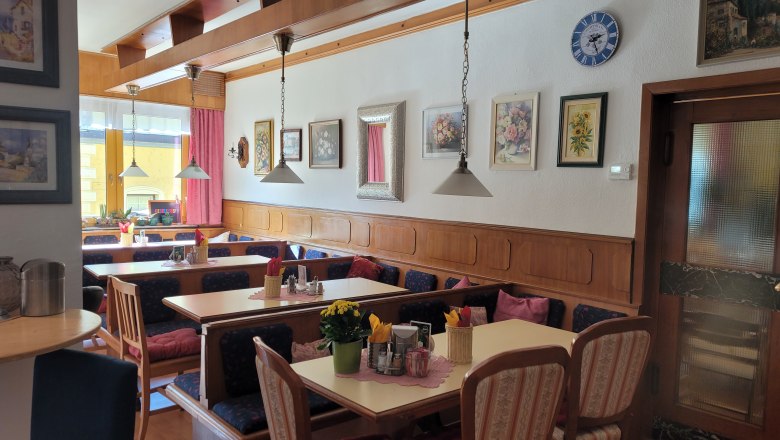 Gemütliche Gaststube mit Holzmöbeln, dekorativen Bildern an der Wand und gedeckten Tischen.