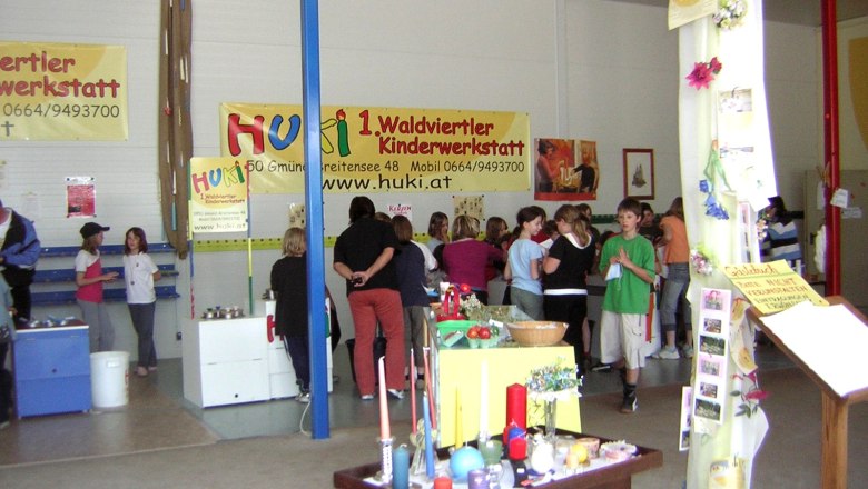 Innenansicht einer Kinderwerkstatt mit Menschen und Bastelmaterialien.