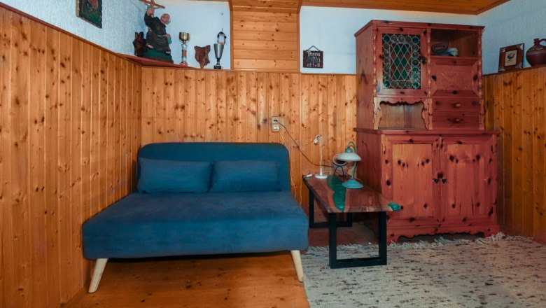 Gem&uuml;tliches Zimmer mit Holzw&auml;nden, einem blauen Sofa, einem Holztisch und einem rustikalen Schrank.