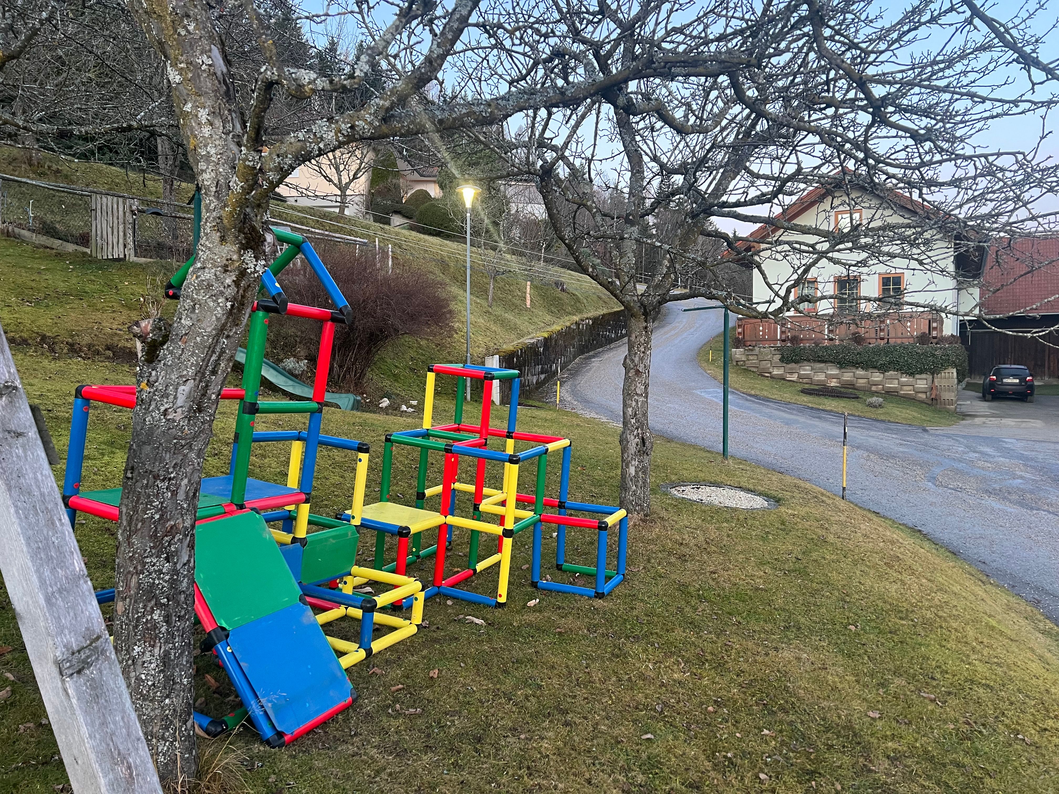 Bunter Kletterspielplatz mit Rutsche auf einer Wiese neben einer Straße und einem Haus.